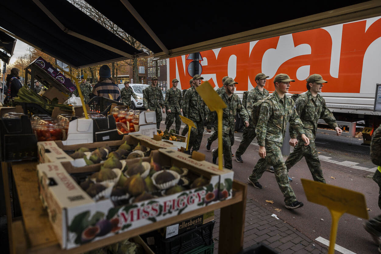 Jonge rekruten marcheren in gelid langs marktkraampjes.
