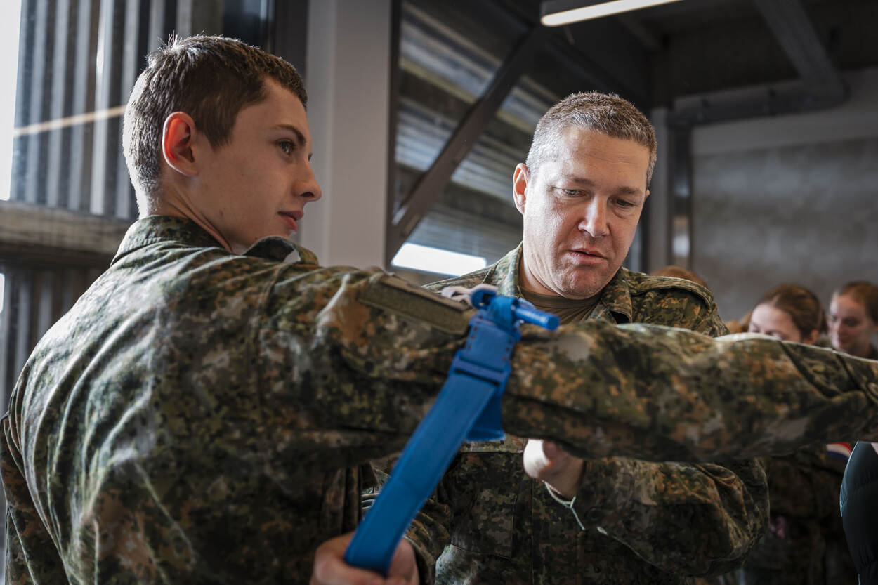 Een militair in opleiding legt een blauwe tourniquet aan op de arm van een collega.