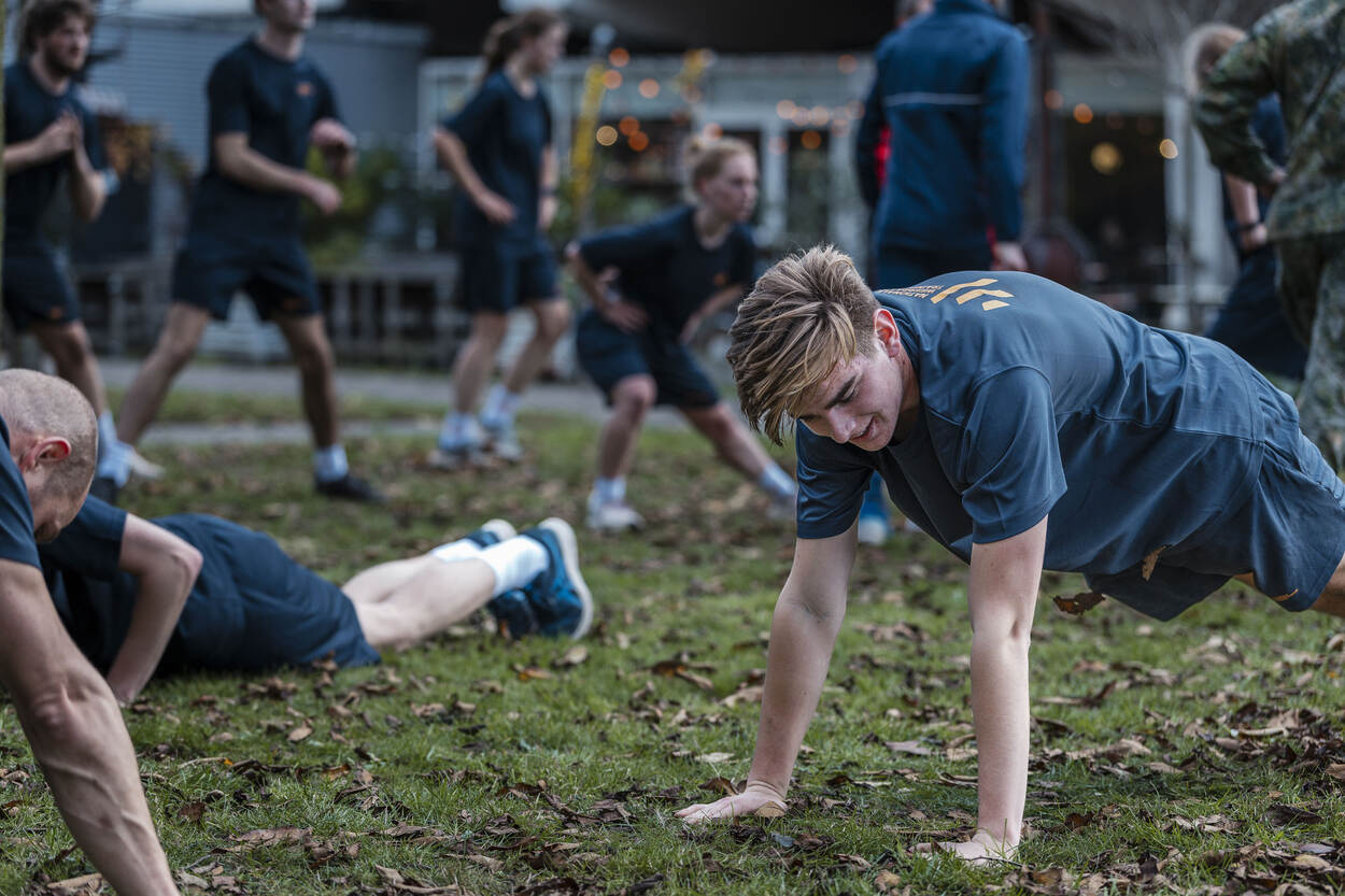 Jonge militairen in blauw sporttenue doen diverse oefeningen met het eigen lichaamsgewicht.