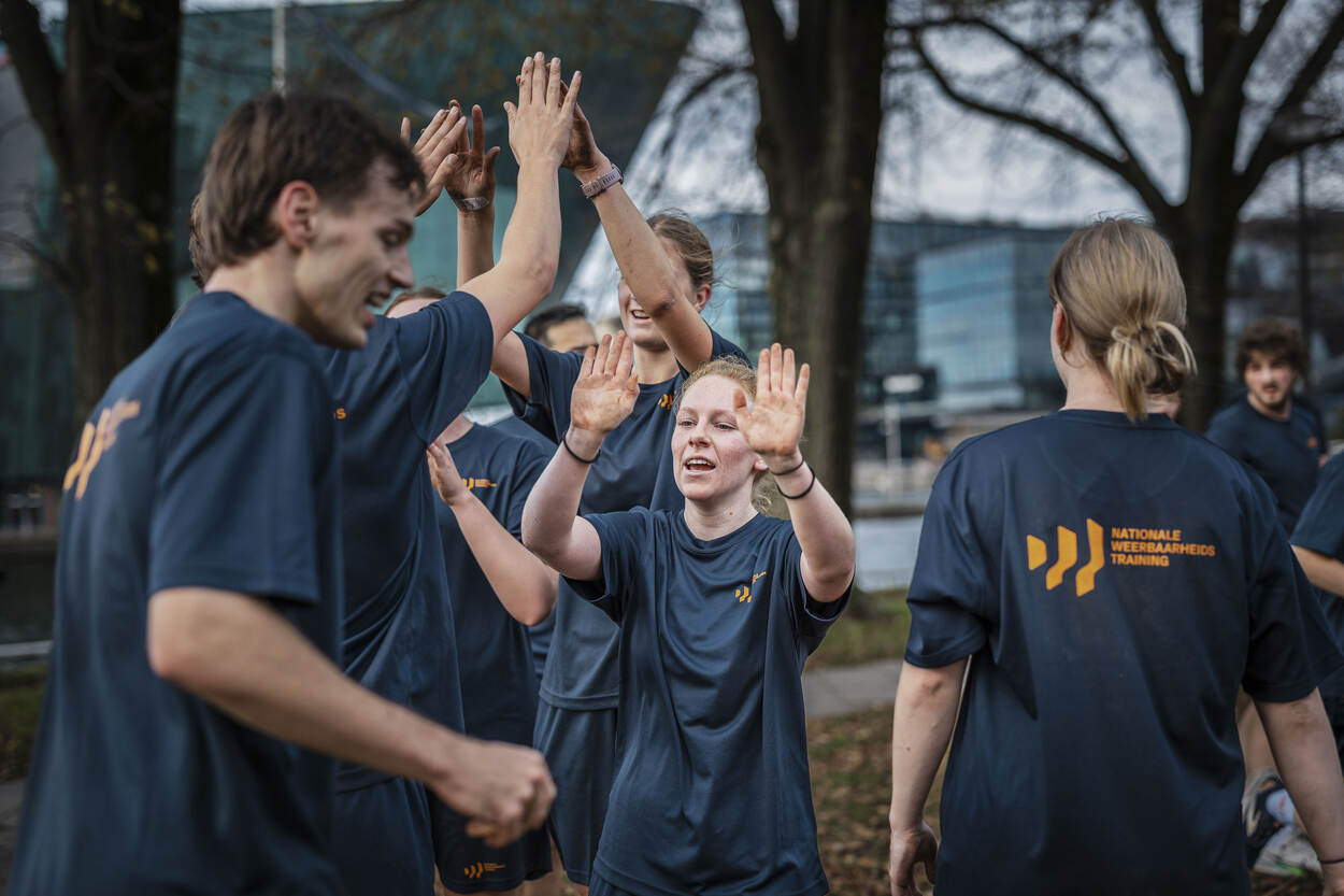 Jonge militairen in blauw sporttenue geven elkaar high fives na een sportles.