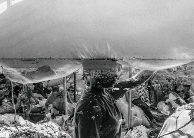 Kayayei (kledingdraagster) op een markt in Accra, tegen de achtergrond van de vervuilde kust.