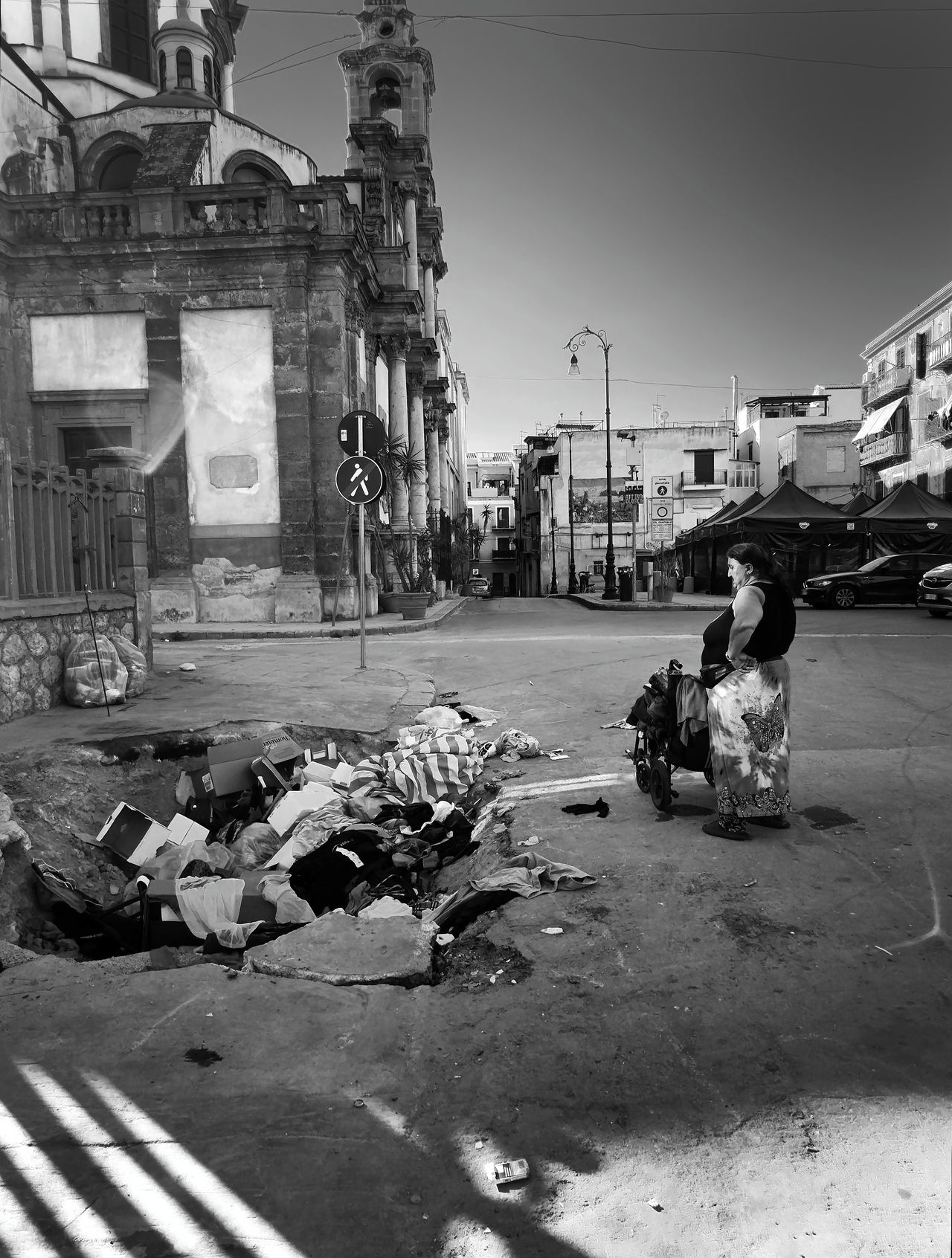Een vrouw kijkt met haar handen in de zij naar een gat in de straat waar het huisvuill in is opgestapeld.  Italie, Palermo 30 mei 2025