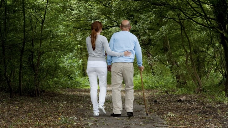 Archiefbeeld van een hulpverlener die een man met wandelstok begeleidt. 
