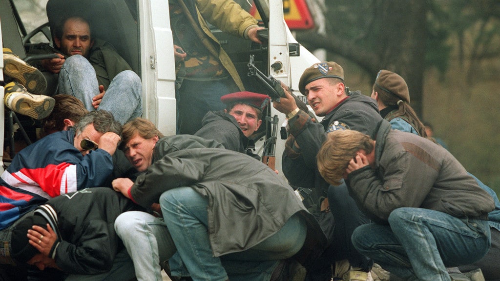 Deze foto, genomen op 6 april 1992, toont een Bosnische soldaat van de speciale troepen (3R) die terugschiet in het centrum van Sarajevo, terwijl burgers proberen te schuilen in een voertuig. 