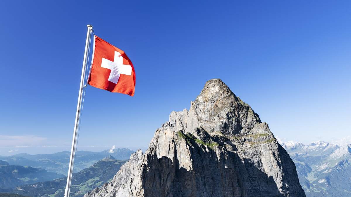Swiss flag with Gstellihorn under a blue sky on a sunny summer day. Bernese Alps, Canton of Bern, Switzerland