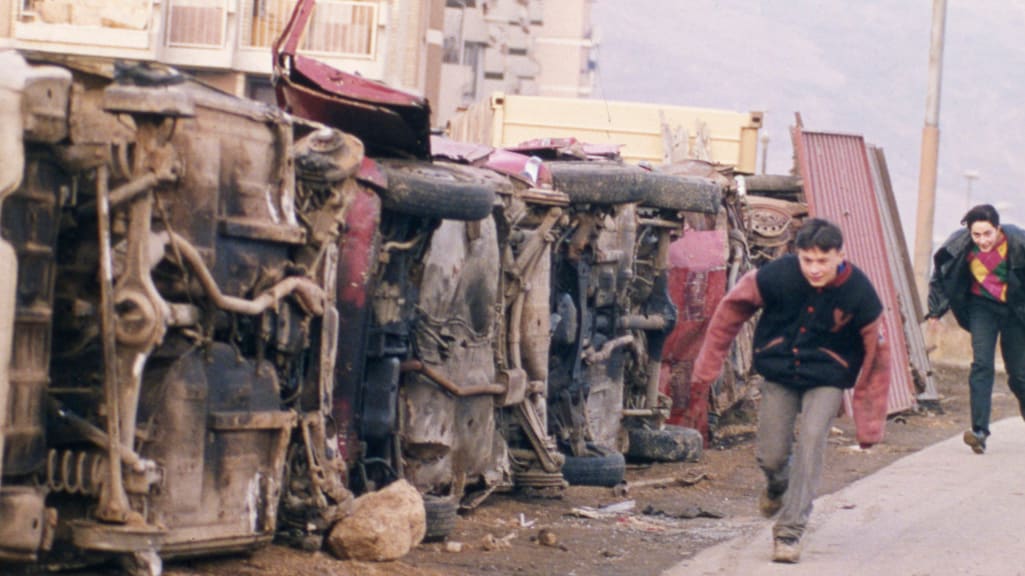 Twee Bosnische jongens zoeken dekking voor sluipschutters achter een muur die is gebouwd van autowrakken in de buitenwijk Dobrinja van Sarajevo, 1993