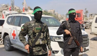 Hamas-leden staan bij een auto van het Rode Kruis. De terreurgroep zegt resten van drie gijzelaars te heben gevonden.
