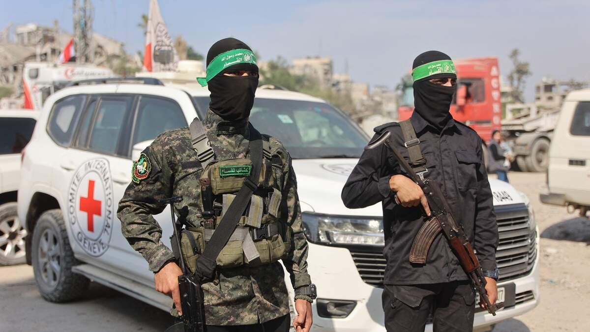 Hamas-leden staan bij een auto van het Rode Kruis. De terreurgroep zegt resten van drie gijzelaars te heben gevonden.