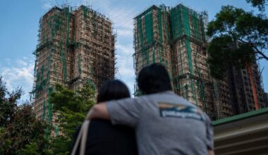 Omstanders kijken naar de uitgebrande woontorens in de wijk Wang Fuk Court in Hongkong.