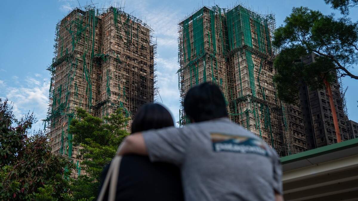 Omstanders kijken naar de uitgebrande woontorens in de wijk Wang Fuk Court in Hongkong.