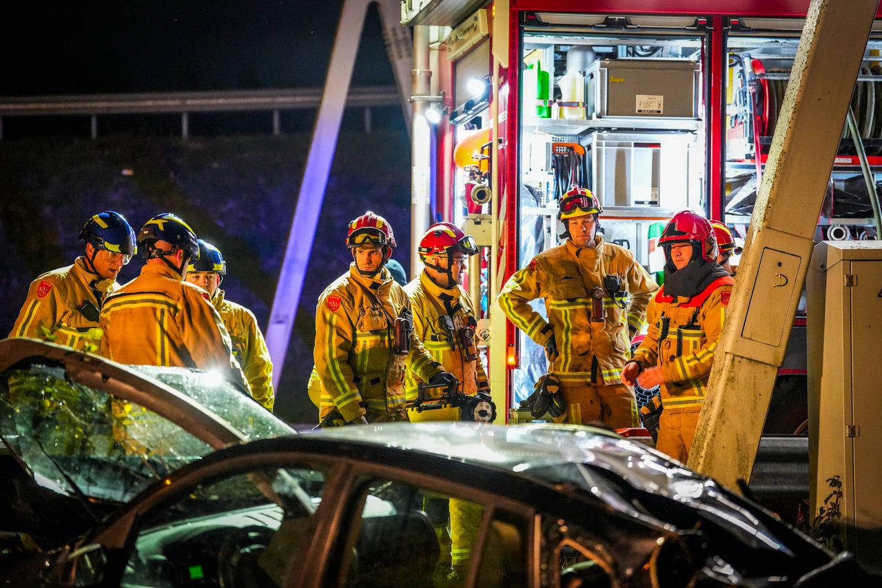 Hulpverleners bekijken de zwaar beschadigde auto na de crash op de A2 bij Eindhoven (foto: Persbureau Heitink).