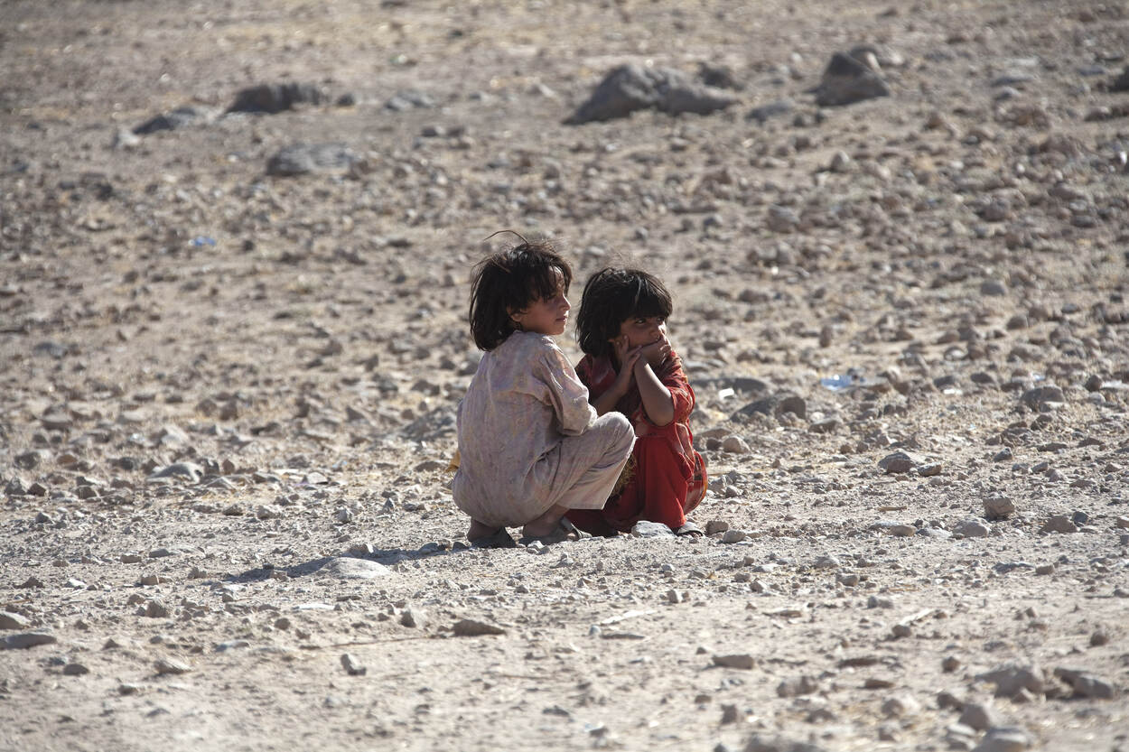 2 jonge kinderen zitten op een dorre vlakte.