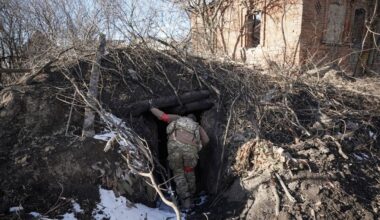 Een soldaat in uniform kijkt in een verlaten schuilplaats die is bedekt door takken.