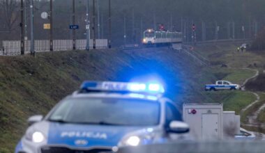 Een politieauto staat met zwaailichten aan voor een spoorlijn op een dijk, waarop een trein stilstaat. 
