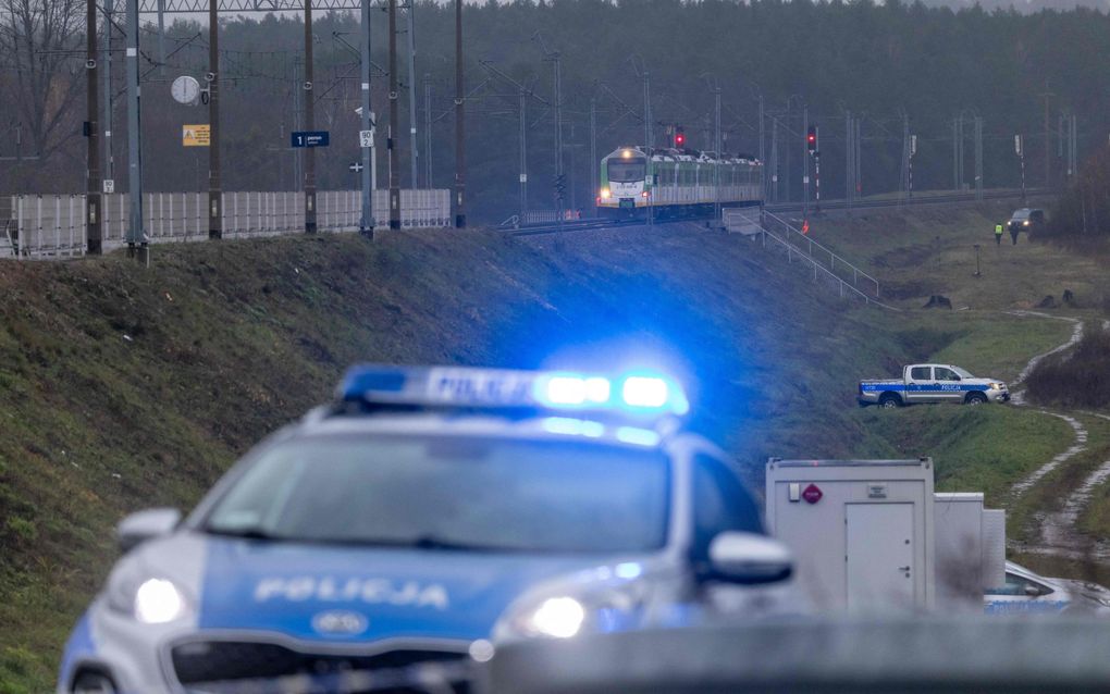 Een politieauto staat met zwaailichten aan voor een spoorlijn op een dijk, waarop een trein stilstaat. 