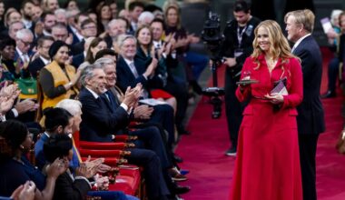 Jonge vrouw in rode jurk laat lachend boekje in glazen stolp zien.