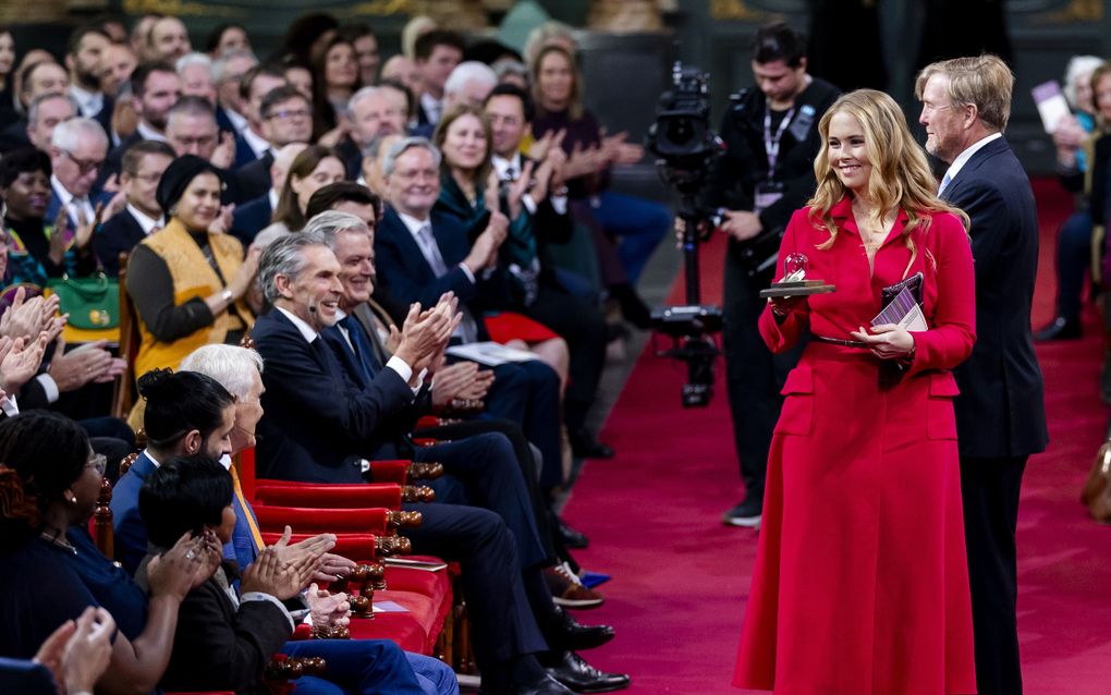 Jonge vrouw in rode jurk laat lachend boekje in glazen stolp zien.