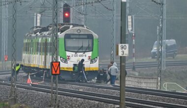Een trein in de kleuren groen, wit en geel staat stil op een spoorweg. Eromheen staan en lopen allerlei mannen.