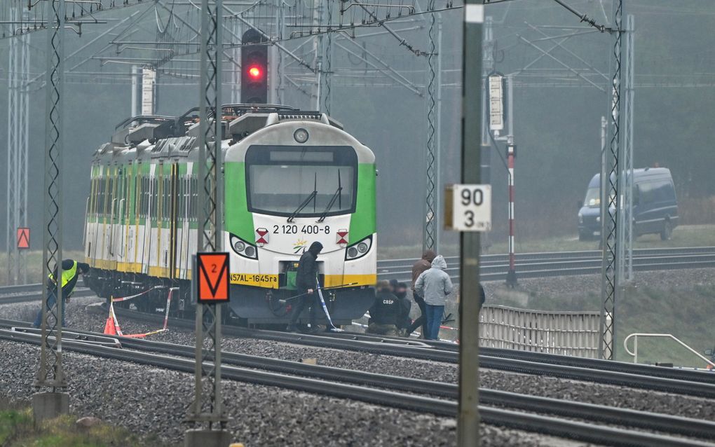 Een trein in de kleuren groen, wit en geel staat stil op een spoorweg. Eromheen staan en lopen allerlei mannen.