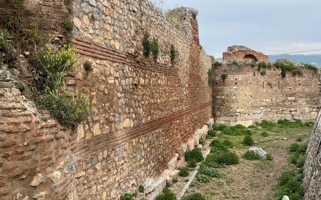 Dikke, deels afgebrokkelde stadsmuren, deels begroeid met onkruid.
