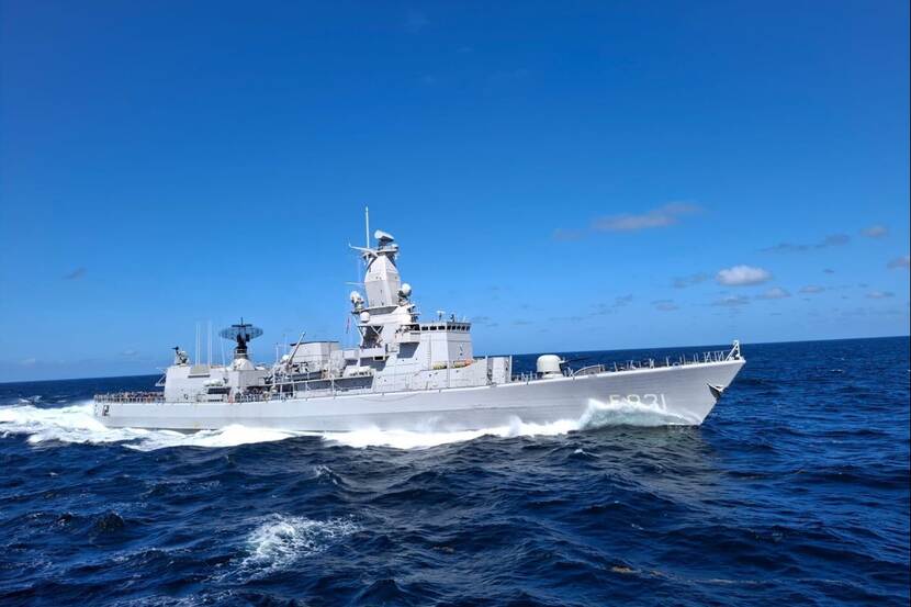 Marineschip vaart door golven tegen blauwe lucht.