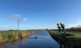Medewerkers van de Dierenambulance halen een dode vogel uit het water in de buurt van Ransdorp bij Amsterdam.