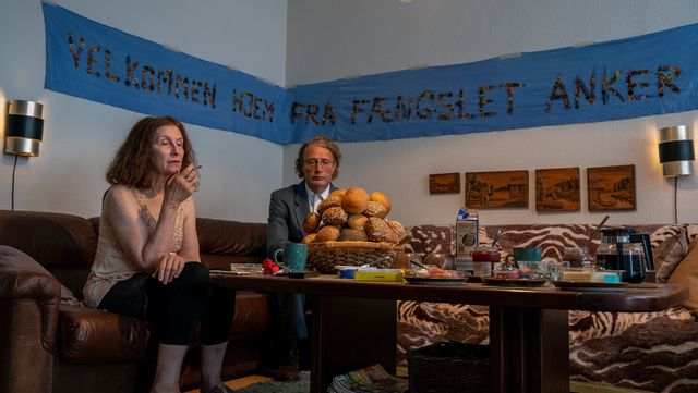 Manfred (Mikkelsen, rechts) onder een spandoek waarop staat: „Welkom terug uit de gevangenis, Anker!”