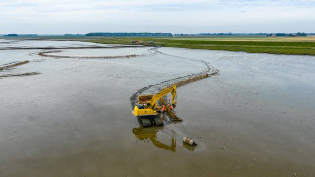 Een graafmachine is bezig met buitendijkse slibsedimentatie bij Termunten.