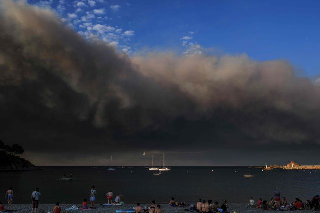 Strandgangers bij het Mediterrane Banyuls-sur-Mer zien op 5 augustus hoe een enorme hoeveelheid rook de Zuid-Franse hemel verduistert, afkomstig van de heftige branden in het Franse departement Aude.
