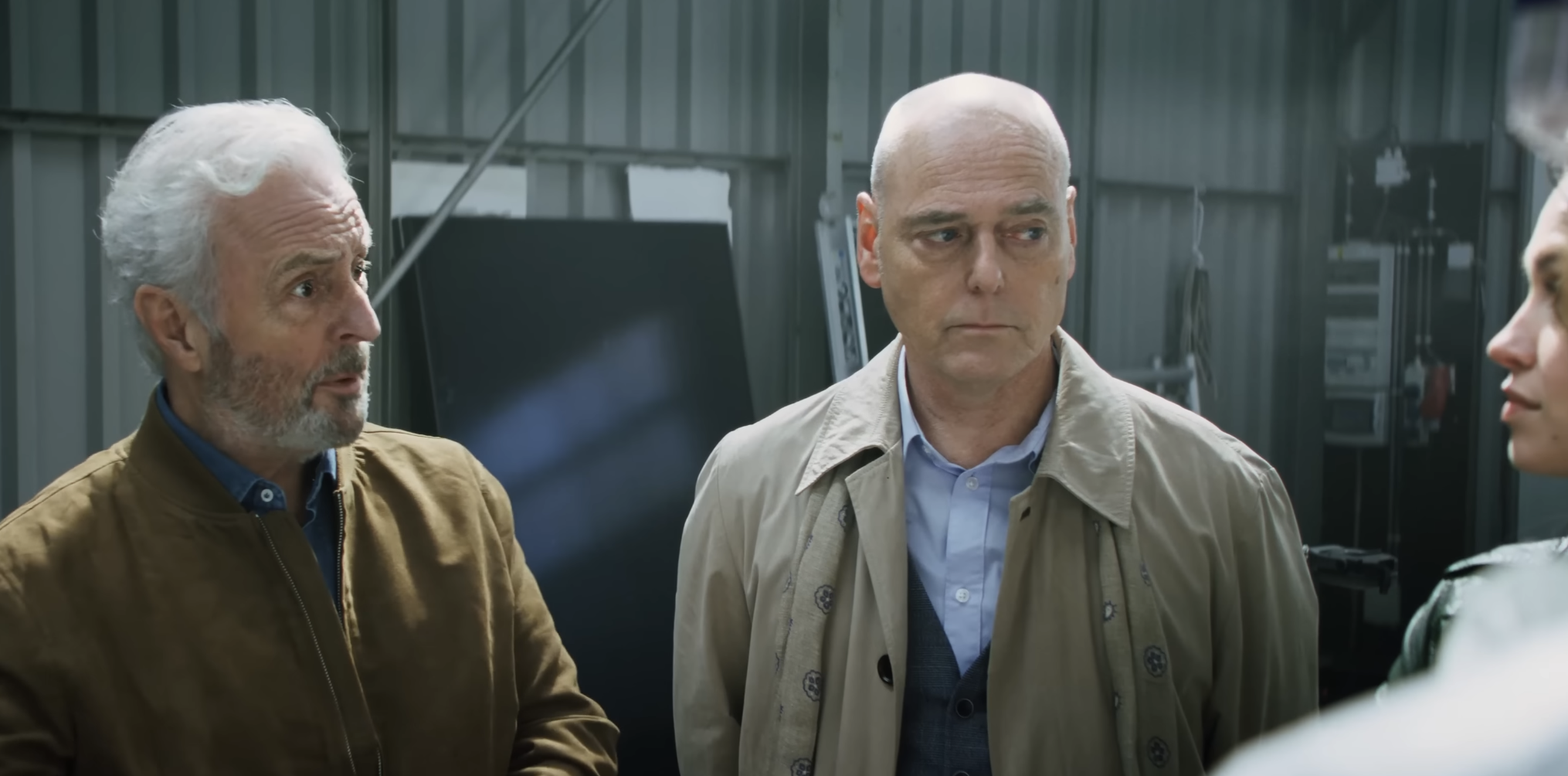 Een afbeelding uit de film Amsterdamned II waarop twee politiemannen staan te praten met vrouwen in een loodsomgeving.