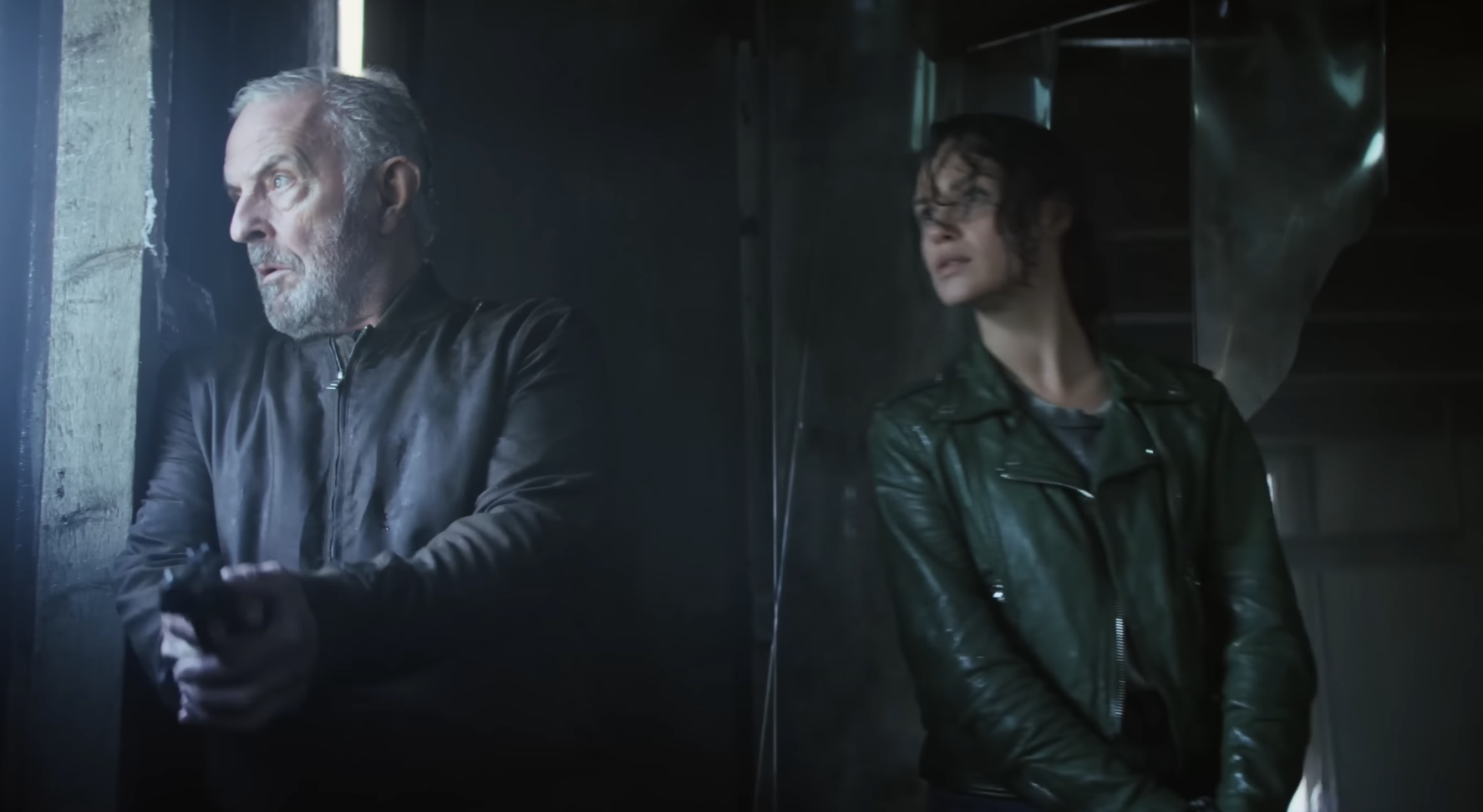 Een afbeelding uit de film Amsterdamned II waarop twee politieagenten, één man en één vrouw, gewapend door een raam naar buiten kijken.