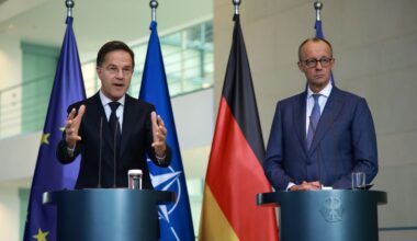 Twee heren in formele kleding achter spreekgestoelte.