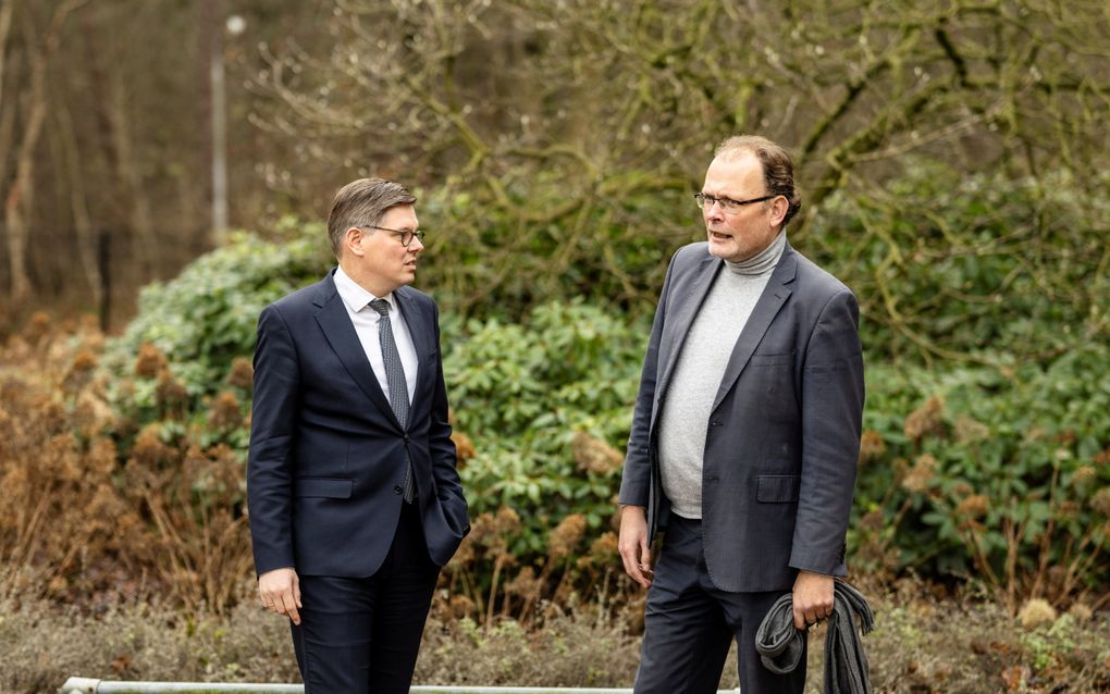 Twee mannen in gesprek. Op de achtergrond struikgewas.