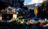 Mensen lopen zondag langs een gedenkplaats met bloemen en kaarsen nabij bar Le Constellation in het Zwitserse Crans-Montana.