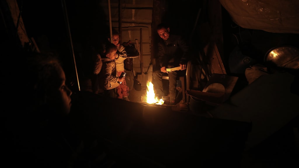 Palestijnse familieleden stoken in een tentenkamp vuur om warm te blijven.