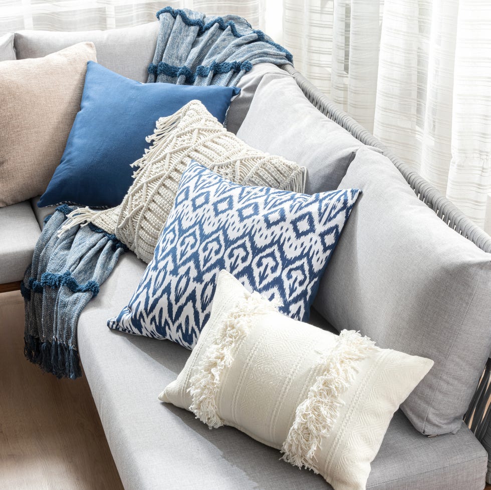 Cozy Living Room Corner with a Soft Grey Sofa Adorned with an Array of Decorative Cushions Various Textures and Patterns, Including Solid Blue, Beige, and a Throw Blanket, Against a Flowing Curtains. cozy living room corner with a soft grey sofa adorned with an array of decorative cushions various textures and patterns, including solid blue, beige, and a throw blanket, against a flowing curtains