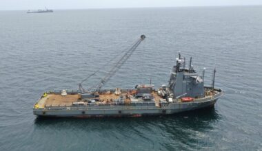 Een grijs schip vaart op zee. Op het ruime achterdek staat een grote kraan.