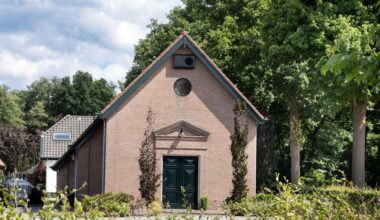 Stenen kerkgebouw met puntdak in bosrijke omgeving.