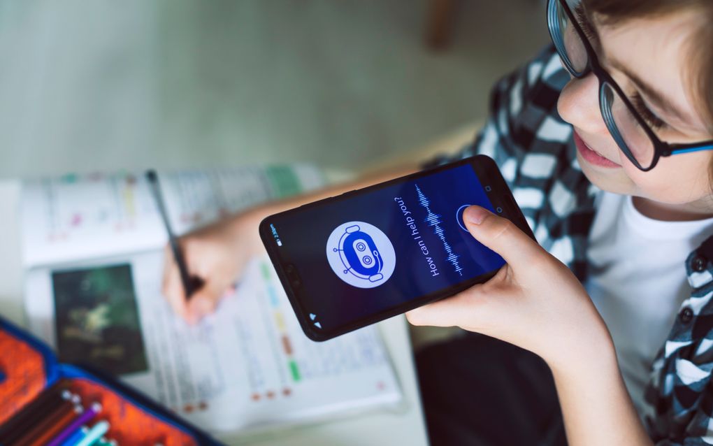 Jongere met een smartphone in zijn linkerhand en een pen in zijn rechterhand, schrijvend aan een tafeltje. 