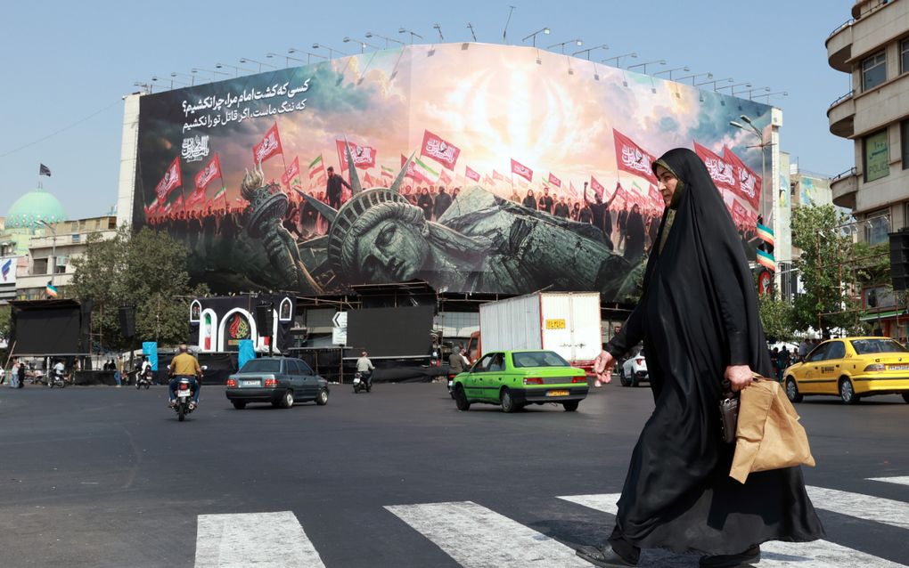 Een gesluierde Iraanse vrouw loopt langs een anti-Amerikaans reclamebord.