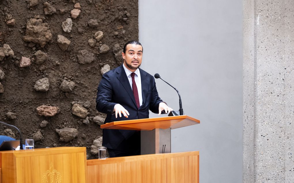 Een man in een pak staat achter het spreekgestoelte van de plenaire zaal van de Tweede Kamer.