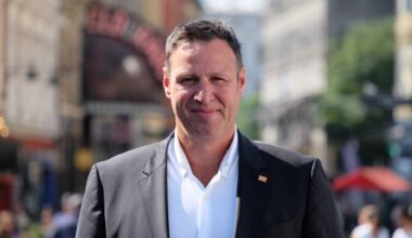 En mann som smiler til kameraet. Han står i en gate med mange folk i bakgrunnen.