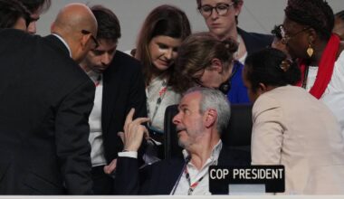 Flere personer samles rundt en bordordfører under en profesjonell diskusjon. En kvinne sitter til venstre med hånd på armen til en annen deltaker. Det er tydelig at de deltar i en viktig samtale knyttet til konferansen. Skiltet "COP PRESIDENT" er synlig på bordet foran dem.