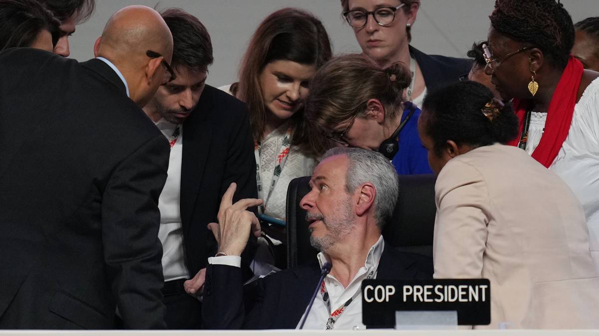 Flere personer samles rundt en bordordfører under en profesjonell diskusjon. En kvinne sitter til venstre med hånd på armen til en annen deltaker. Det er tydelig at de deltar i en viktig samtale knyttet til konferansen. Skiltet "COP PRESIDENT" er synlig på bordet foran dem.