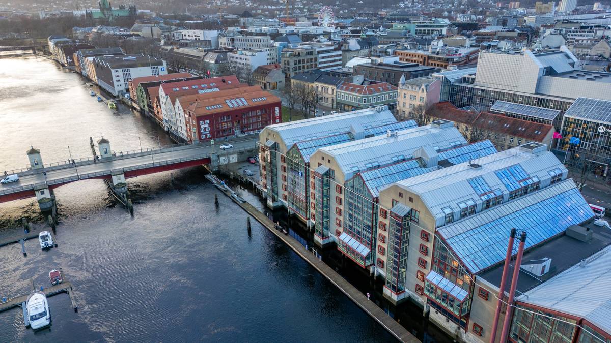 Bilde av en byutsikt over en elv med bygninger langs bredden. Det er en bro i midten som forbinder de to sidene. Flere båter er synlige i vannet, samt en karusell bak bygningene. Området har moderne og historiske bygninger, med trær synlige i bakgrunnen.