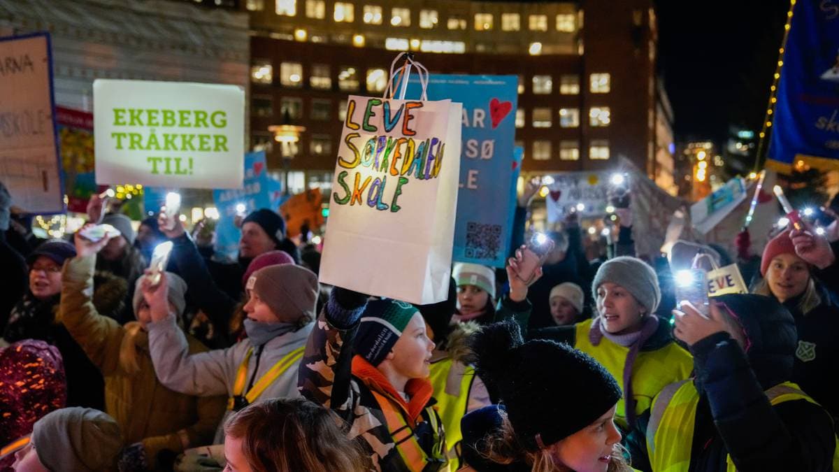 En folkemengde deltar i en demonstrasjon om skolesaker. Flere personer holder opp plakater med budskap som "Leve Særdalskole" og "Ekeberg trekker til!". Deltakerne er kledd i varme klær og enkelte har reflekser på. Det er mørkt, men flere mobiltelefonlysdioder lyser opp scenen.