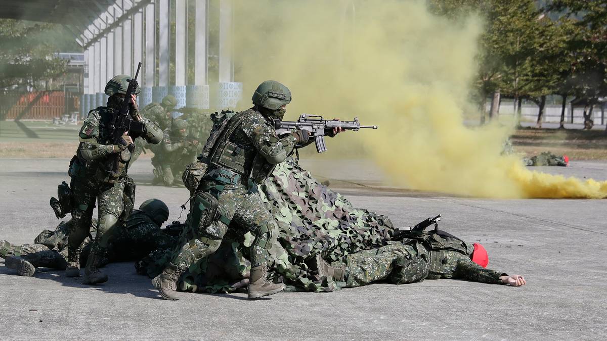 Soldater i kamuflasje deltar i trening med røyk granater. En soldat holder gevær, mens andre tar dekning. Omgivelsene viser et militært treningsområde. Gult røyk legger seg i luften, som bidrar til treningssituasjonen.