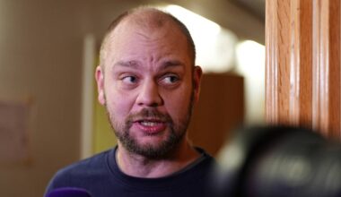 Mimir Kristjansson står foran et kamera, iført en mørk genser. Det er innredning med treverk og dæmpet belysning i bakgrunnen. Mikrofonen rettes mot personen, som ser ut til å snakke. Fokus er på personens overkropp og uttrykk.