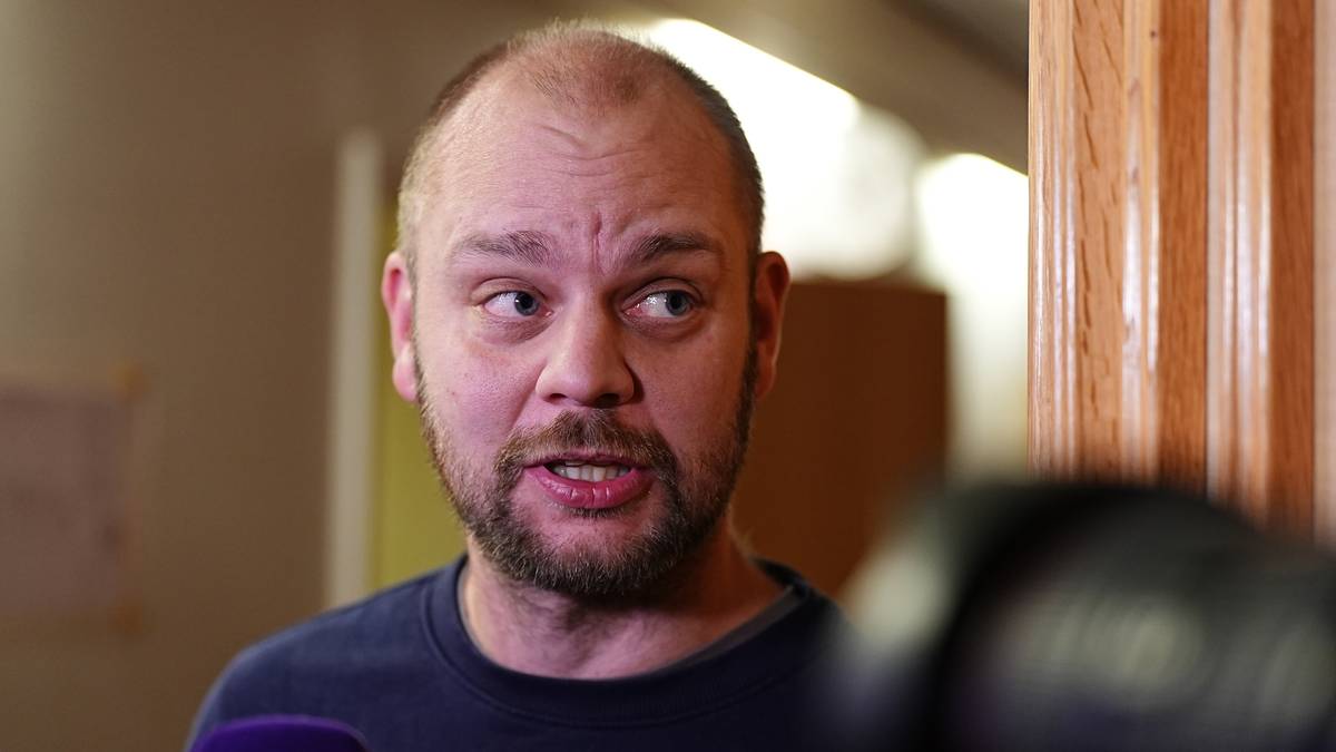 Mimir Kristjansson står foran et kamera, iført en mørk genser. Det er innredning med treverk og dæmpet belysning i bakgrunnen. Mikrofonen rettes mot personen, som ser ut til å snakke. Fokus er på personens overkropp og uttrykk.