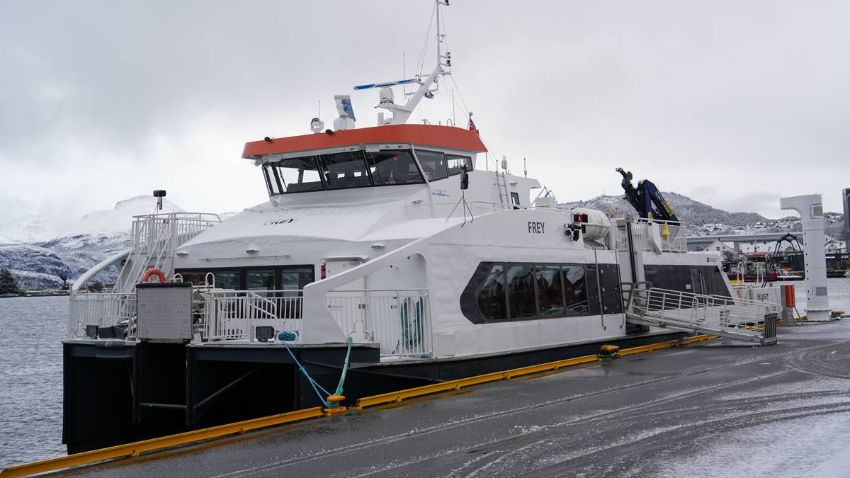 Fergen "Frey" ligger ved kaien i en havn med snødekte fjell i bakgrunnen. Det er grå himmel, og det synes å være kaldt vær. En person er synlig ved fergen, trolig i ferd med å gjøre forberedelser. Kaien er utstyrt med guldkledde stropper og utstyr for lasting av varer.